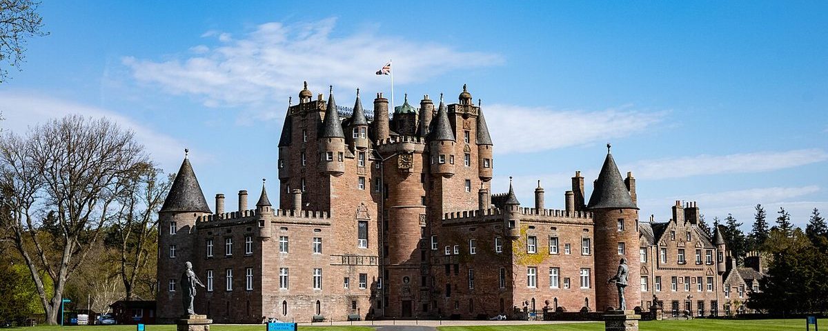 Glamis Castle in Angus, Scotland, a reddish sandstone castle with many turrets and a central tower, seen across a lawn from the approach drive