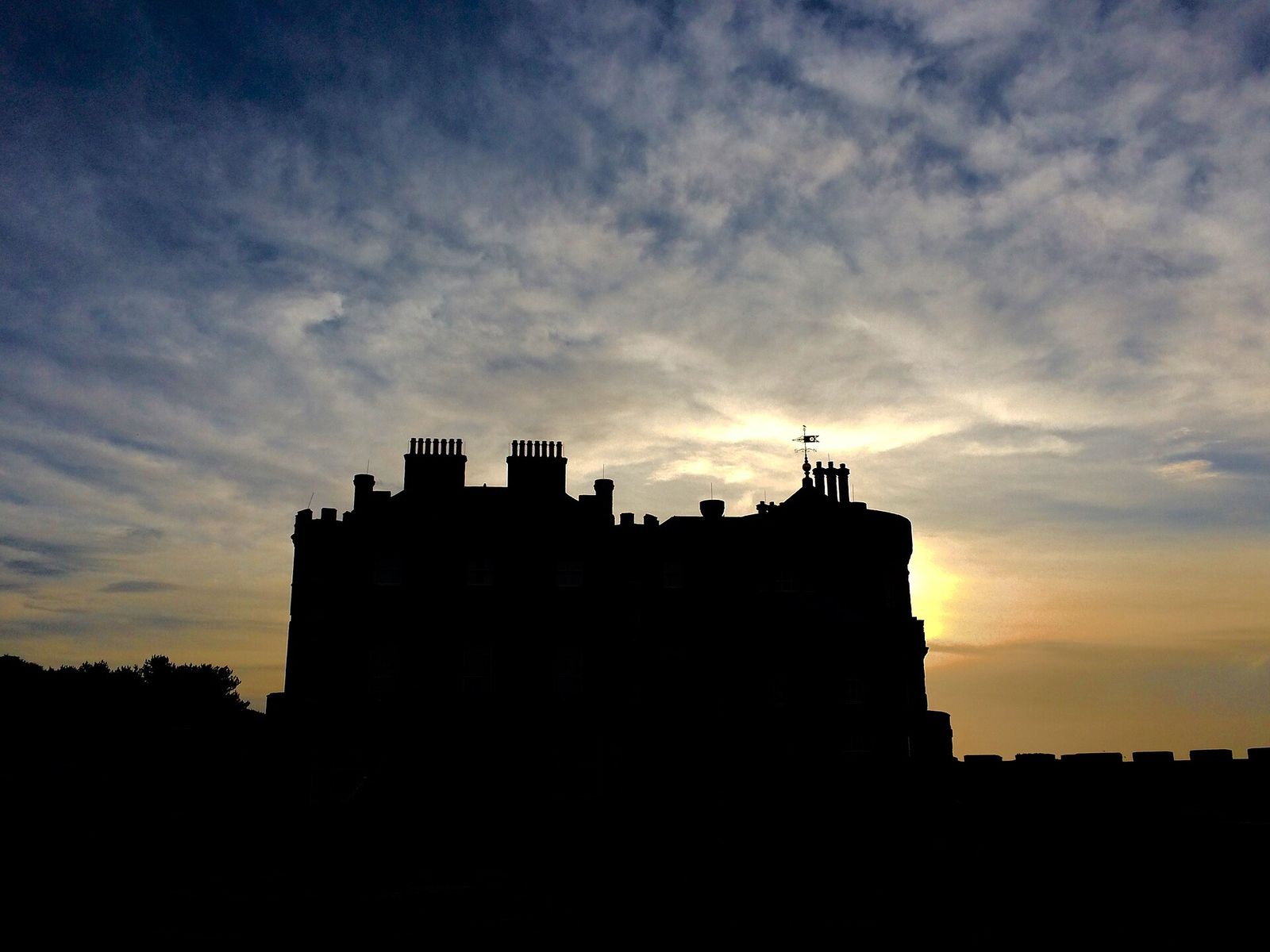 Culzean Castle in silhouette against a cloudy dusk sky, its chimneys and weathervane outlined by the setting sun